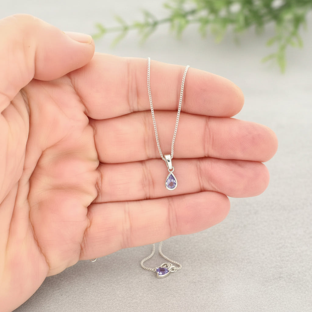 Silver necklace with a teardrop-shaped pendant held in a hand against a white background