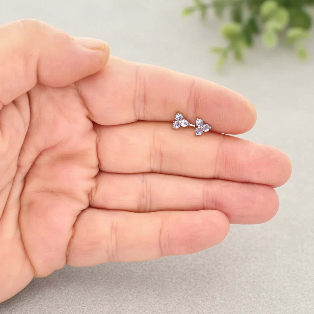 Small flower-shaped earrings held between fingers against a white background
