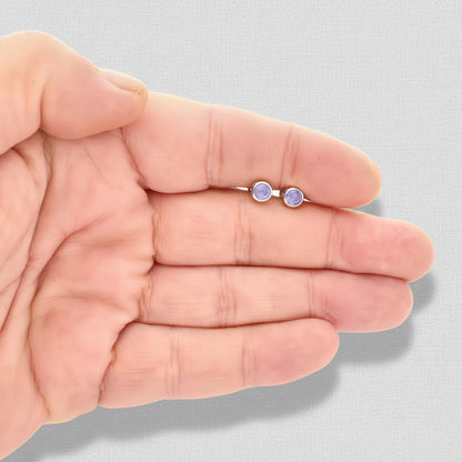 Small round earrings held in a hand against a white background