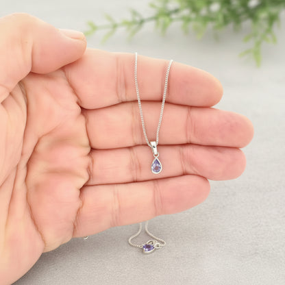 Silver necklace with a teardrop-shaped pendant held in a hand against a white background