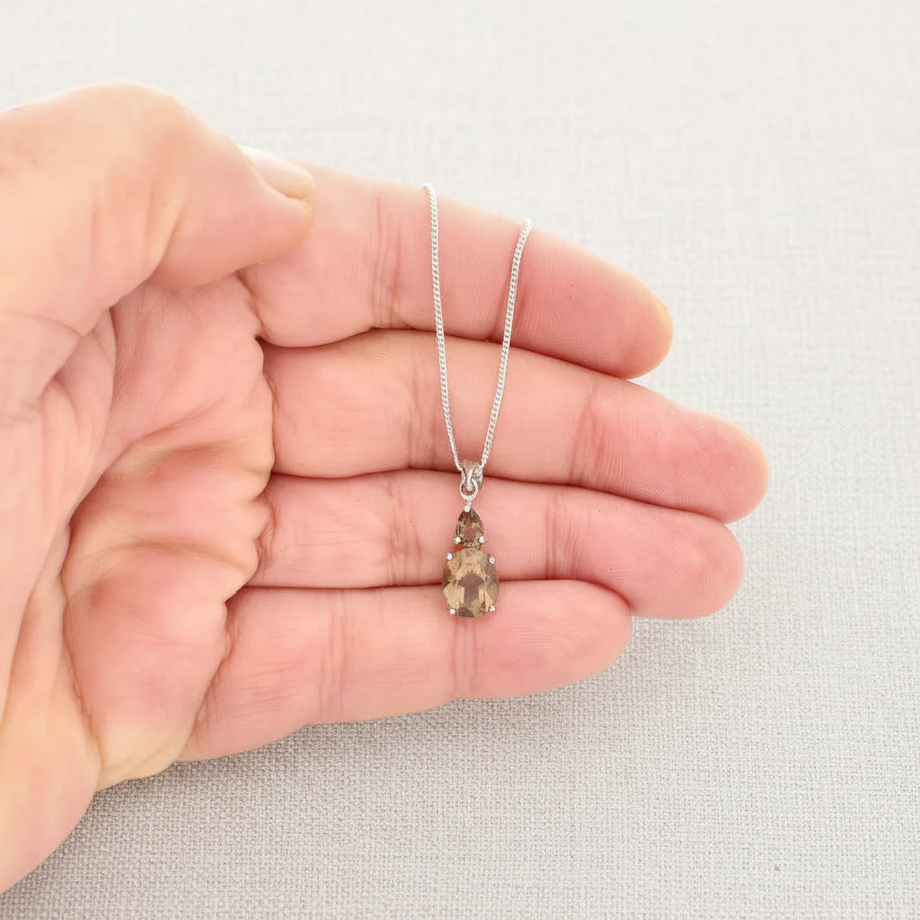 Hand holding a silver necklace with a teardrop-shaped pendant against a white background