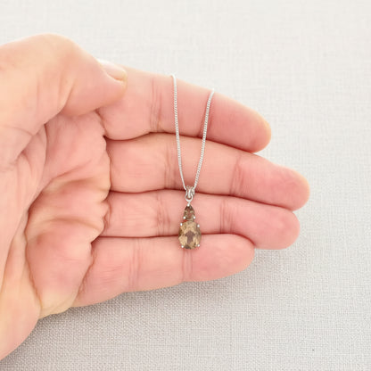 Hand holding a silver necklace with a teardrop-shaped pendant against a white background